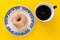 A cup of coffee and a plate with sugar coated doughnut, on yellow background