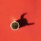 A cup of coffee on red surface with steam. Shadow in shape of zodiac ox horns