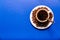 Cup of coffee, saucer with coffee beans and a spoon on a blue background