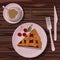 Cup of coffee on saucer, piece of cherry pie on pink ceramic plate isolated on wooden table.