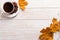 Cup of coffee with scattered coffee beans, dry yellow leaves on a wooden table. Autumn morning mood, copy space