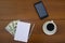 Cup of coffee, smartphone, dollars, notepad and pen on wooden desk