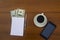 Cup of coffee, smartphone, dollars, notepad and pen on wooden desk