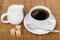 Cup of coffee with spoon, pieces sugar and milk jug