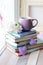 Cup of coffee, a stack of books decorated with hearts, apple flowers on a wooden windowsill