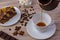 A cup of coffee and a tasty cake on a saucer. Chocolate bar, coffee beans, a bowl with sugar cubes, and anise on bright wooden bac