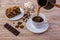 A cup of coffee and a tasty cake on a saucer. Chocolate bar, coffee beans, a bowl with sugar cubes, and anise on bright wooden bac