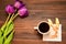A cup of coffee or tea with a croissant on a napkin stands on a wooden background, next to it are purple tulips