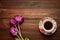 A cup of coffee or tea on a saucer stands on a wooden background, purple tulips lie next