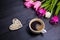 Cup of coffee, wicker heart and bouquet of tulips on black wooden background