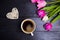 Cup of coffee, wicker heart and bouquet of tulips on black wooden background