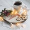 A cup of coffee on a wooden stand, gingerbread cookie tied with a rope, a garland on the table. Artificial spruce branch with