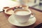 Cup of coffee on wooden table with blur plate of brownie at background.