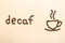 Cup of coffee and word Decaf made with beans on beige background, flat lay