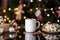 Cup of delicious hot cocoa with cookies and Christmas decorations on table against blurred lights