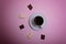 A cup of espresso coffee, pieces of chocolate on a pale pink background.