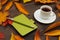 Cup of espresso, green notebook and pen among autumn fallen leaves