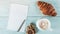 Cup of fresh coffee with croissant on wooden background and a notebook page for your text, selective focus