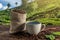 Cup of fresh coffee and roasted beans in a bag on the table against the backdrop of a landscape of coffee plantations