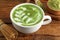 Cup of fresh matcha latte and bamboo whisk on wooden table, closeup