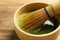 Cup of fresh matcha tea with bamboo whisk on wooden table, closeup