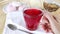 Cup of fruit tea is placed on table. Hibiscus in glass transparent mug. Bright red hot drink, compote. Summer tea break with