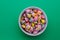 Cup full of colorful pieces of hard tack rainbow candy on a green background