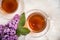 A cup of green tea against the background of a spring bouquet of lilacs on a textured background.