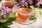 A cup of green tea against the background of a spring bouquet of lilacs on a textured background.