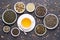 Cup of green tea and bowls of various dried tea leaves on dark, stone background