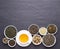 Cup of green tea and bowls of various dried tea leaves on dark, stone background