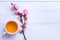 Cup of green tea and branches of blossoming peach on lilac wooden table