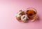 A cup of green tea and three profiteroles sprinkled with sugar powder on a pink background.