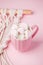 Cup of hot chocolate with pink heart shaped marshmallows and macrame panel on pink background, trendy minimal romantic composition