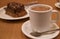 A cup of hot chocolate with a plate of blurry chocolate cake served on wooden table