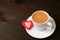 Cup of hot coffee with a heart shaped cookie on dark brown wooden table