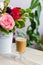 Cup of hot coffee with milk stands near the window and a bright colored bouquet of flowers