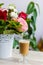 Cup of hot coffee with milk stands near the window and a bright colored bouquet of flowers