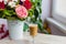 Cup of hot coffee with milk stands near the window and a bright colored bouquet of flowers