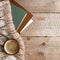 Cup of hot coffee on rustic wooden table, books, closeup photo warm sweater with mug, winter morning concept, top view, moody