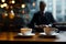 Cup of hot coffee with saucer on table, businessman seated