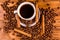 Cup of hot coffee, star anise, cinnamon sticks and scattered coffee beans on wooden table. Top view