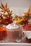 Cup of hot creamy cocoa with froth on the white tray with autumn leaves and pumpkins on the background