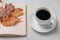 Cup of hot drink, book and autumn leaves on light grey textured table