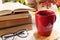 Cup with hot drink, stack of books and glasses on white wooden table. Autumn atmosphere