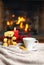 Cup of hot drink teddy bear candle in red Christmas decoration on cozy knitted plaid in front of warm fireplace. Holiday Christmas
