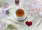 A Cup of hot tea in a white Cup on a knitted white sweater with a red heart, a garland, branches of thuja, cones, top view-the