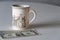 A cup with an image of an old house is on the table, several American banknotes are lying nearby