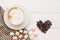 A cup of Latte Art coffee, design with marshmallow, heart-shaped love on fabric and roasted coffee beans on a white wooden table