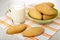 Cup with milk, shortbread cookies in green bowl and on napkin on wooden table
